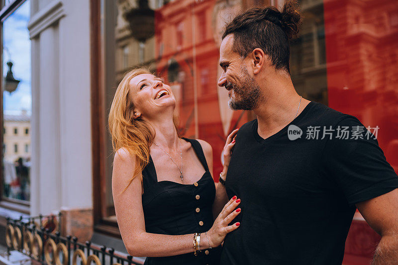 Young redhead European woman laughing touching boyfriend outdoors. Handsome Hispanic  man dating with girl on valentine's day. Pretty American girl giggling after fiancÃ©âs joke. Romance, honeymoon.